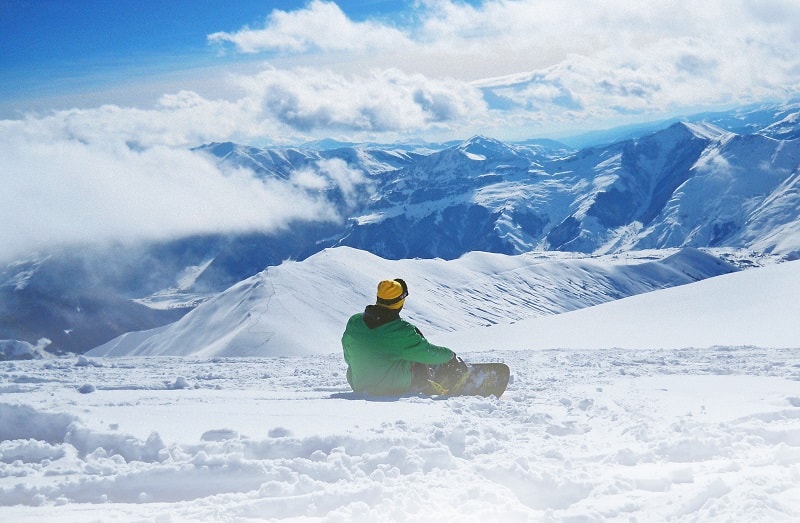 man on a snowboard sitting alone on the mountain